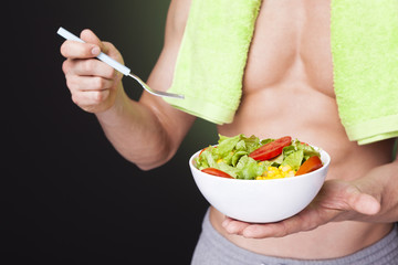 Closeup of a fit man holding a bowl of fresh salad on dark backg
