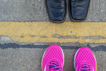 Black leather shoes and pink running shoes on road background
