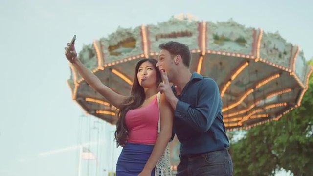 A couple taking selfies in front of a carnival ride