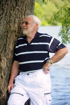 Senior lehnt sich an einen Baum am See