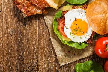 Sandwich with a fried egg, bacon, cheese and vegetables.