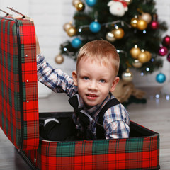 Little boy playing hiding in a red plaid suitcase in the interio