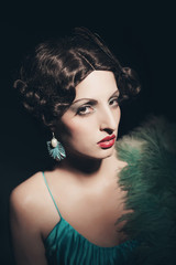 Glamour retro 1920s young woman holding a fan. Against black bac