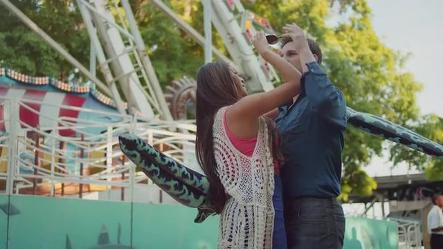 A couple embracing and being silly in front of a carnival ride
