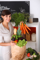 Happy young woman holding bunch of carrots in kitchen