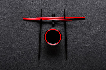 Chopsticks and bowl with soy sauce on black stone background