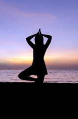 Fototapeta premium Silhouette young woman practicing yoga on the beach at sunset.