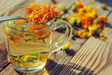 Herbal tea from flowers of a marigold in a transparent glass mug. Medicinal flowers of a calendula.