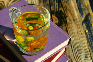 Herbal tea from flowers of a marigold in a transparent glass mug on old books on a wooden surface. Medicinal flowers of a calendula.