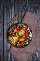 Fried snails with garlic butter and herbs on dark background