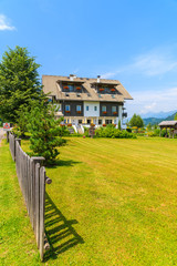 Wooden fence on green meadow and view of typical alpine house in summer landscape of Alps Mountains, Weissensee lake, Austria