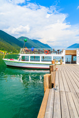 Tourist boat mooring to pier on shore of Weissensee lake in summer landscape of Alps Mountains, Austria