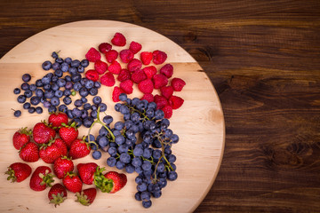 Strawberries, raspberries,  blueberries and grapes on wooden plate