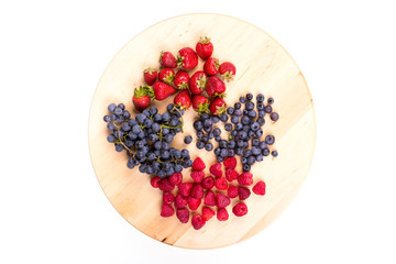 Strawberries, raspberries,  blueberries and grapes on wooden plate