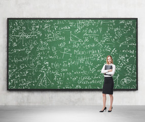 Full length of nice lady who holds black folder and stands in front of the green chalkboard, which...
