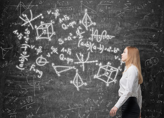 Young lady is looking at the green chalkboard with math formulas.