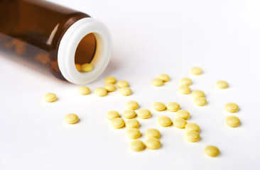 Yellow Pills spilled from a bottle on white surface