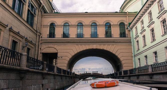 view from passenger boat as it moves through narrow canal under the passage connecting the Hermitage Museum palaces 