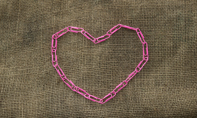 pink paper clips arranged in heart shape on jute background.