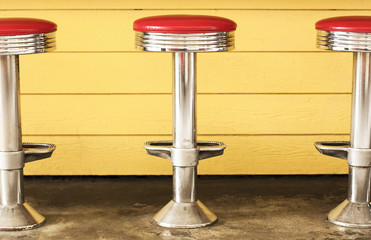 Three retro chrome diner stools.  Red vinyl seats, yellow background