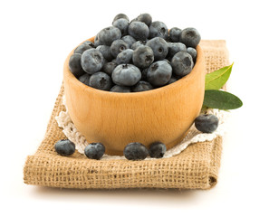 Blueberries in the wooden bowl with green leaves on the burlap c
