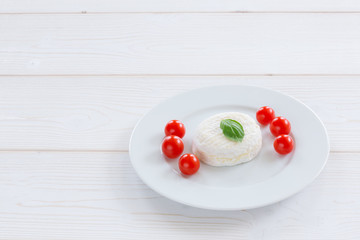 Camembert round entirely with cherry tomatoes and basil leaf on a white plate and a white wooden background