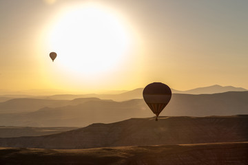 Two ballons in front of big sun over mointains and rocks in cappadocia