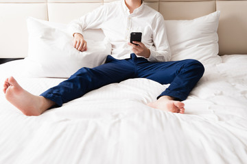 ベッドルームでスマートフォンを操作する日本人男性