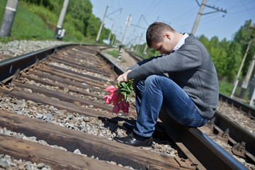 Sad man with flowers sitting on the rails
