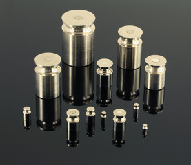 Set of iron weights on light (almost white) surface with chessboard background. Hemi-transparent surface shows chess board background. 