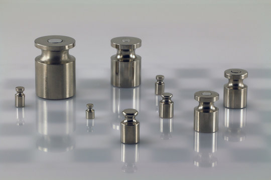 Set of iron weights on light (almost white) surface with chessboard background. Hemi-transparent surface shows chess board background. 