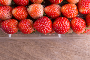 red ripe strawberry in plastic box of packaging on wood table