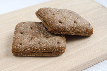 two pieces of rye bread square shape and rye bran and muesli on plates on wood background with selective focus