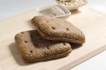 two pieces of rye bread square shape and rye bran and muesli on plates on wood background with selective focus