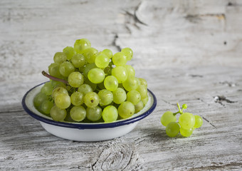 fresh green grapes in a white enamel bowl on a light wooden surface