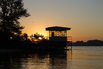 Silhouette of the house on the river bank at sunset