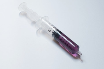 syringe with purple liquid on light background