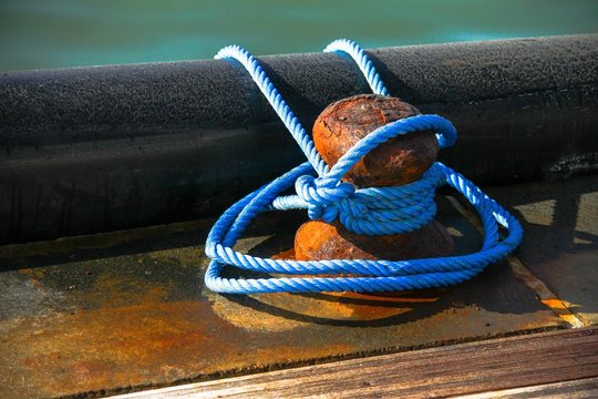 Close-up of mooring bollard with blue rope in marina