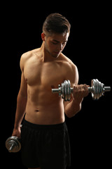 Fototapeta na wymiar Muscle young man holding dumbbells on dark background