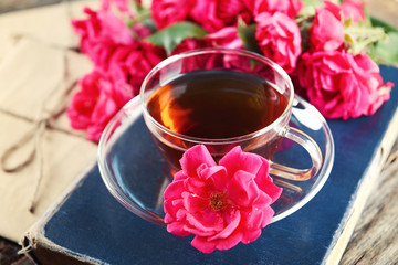 Old book with beautiful flowers and cup of tea on wooden table close up