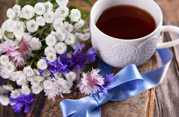 Old book with beautiful flowers and cup of tea on wooden table close up