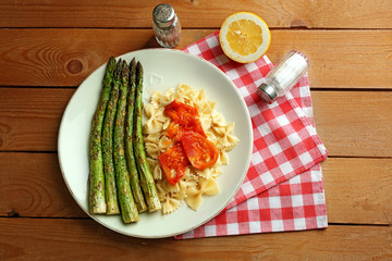 Roasted asparagus and tasty pasta with vegetables on plate on wooden table background