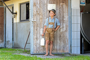 Junge in Lederhose am Milchhaus mit Milchkanne