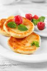 Fritters of cottage cheese with raspberries in plate on table, closeup