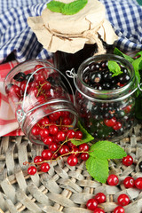 Ripe forest berries in glass jar and tasty jam on wooden background