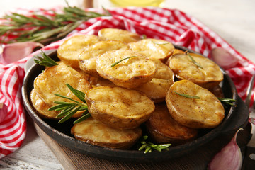 Delicious baked potato with rosemary in frying pan on table close up