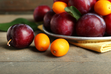 Ripe plums in metal plate on wooden table, closeup