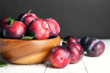 Ripe plums in bowl on wooden table on dark background