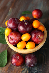 Ripe plums in bowl on wooden background