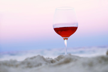 Romantic glass of wine sitting on the beach at colorful sunset